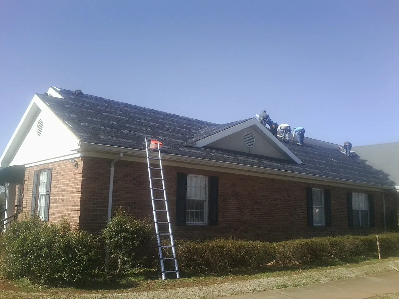Crew tearing shingles off a brick ranch roof with a ladder set — Emergency Roof Repair work by our crew in Salisbury