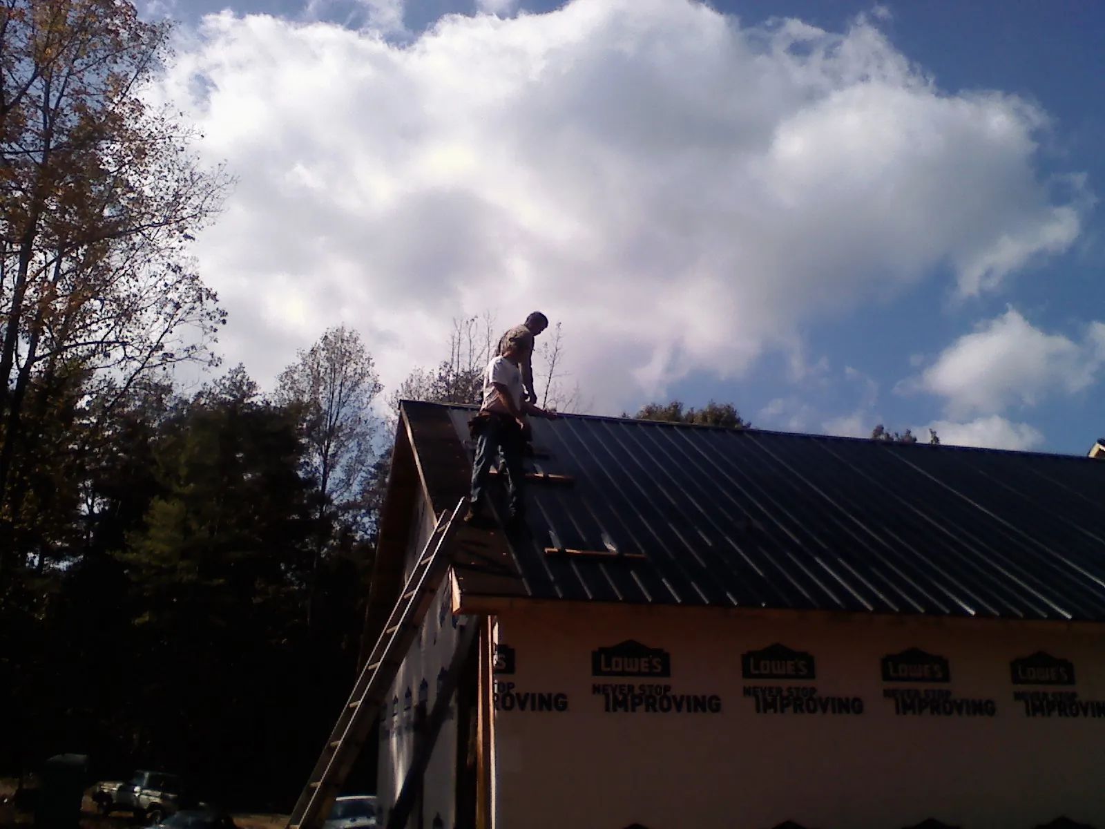 Roofer fastening dark metal panels high against a cloudy sky, from a Roof Inspection job in Salisbury